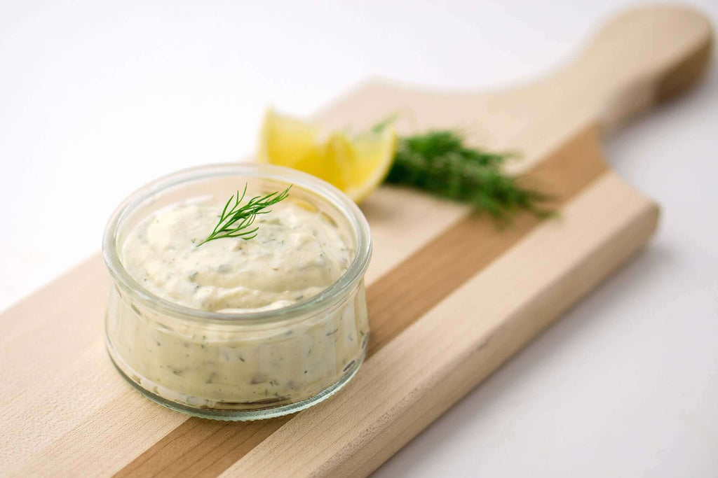 Preserved lemon aioli in a glass jar garnished with dill, served on a wooden cutting board with lemon wedges.