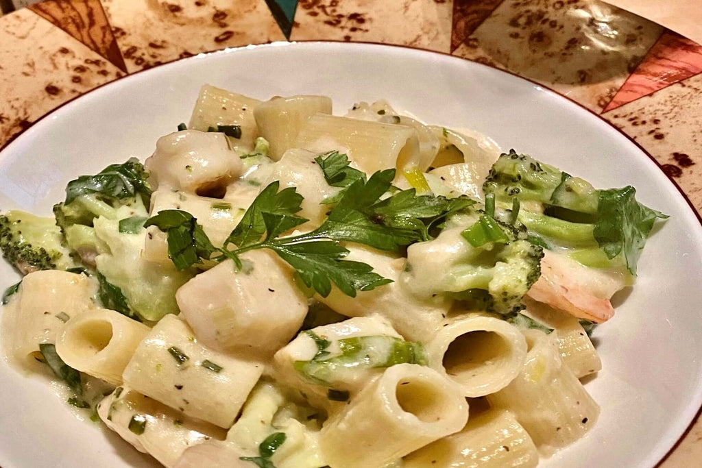 Creamy seafood Alfredo pasta with broccoli and herbs, garnished with fresh parsley in a decorative bowl.