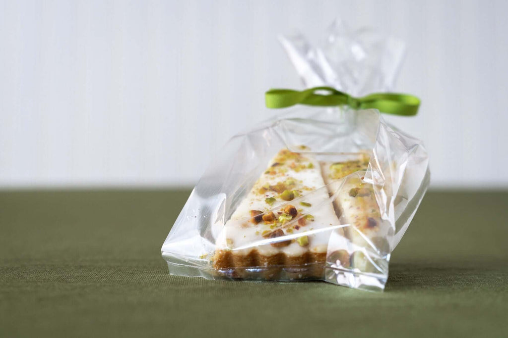 Wrapped pistachio shortbread cookies tied with a green ribbon on a green background.