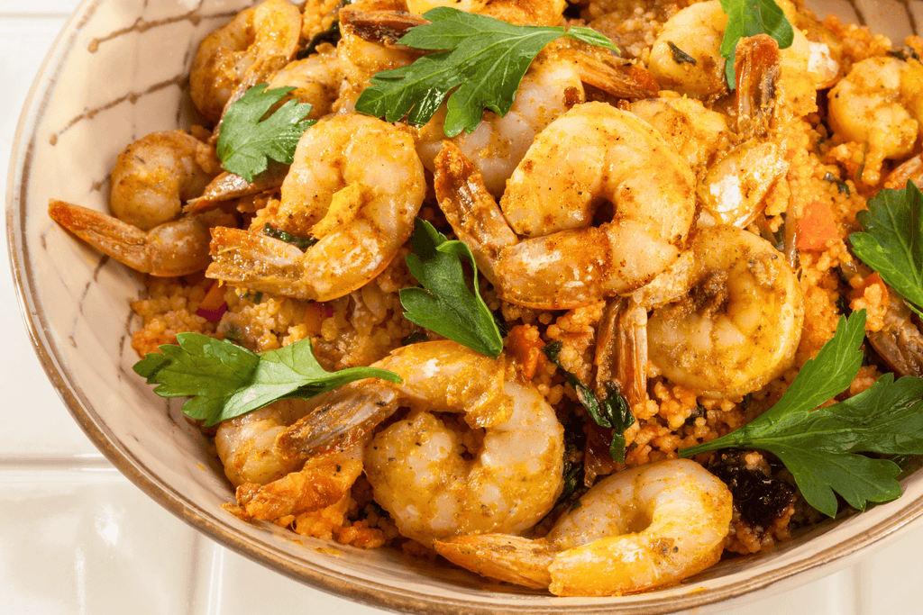 Moroccan-spiced shrimp with couscous and quinoa, garnished with fresh parsley in a decorative bowl.