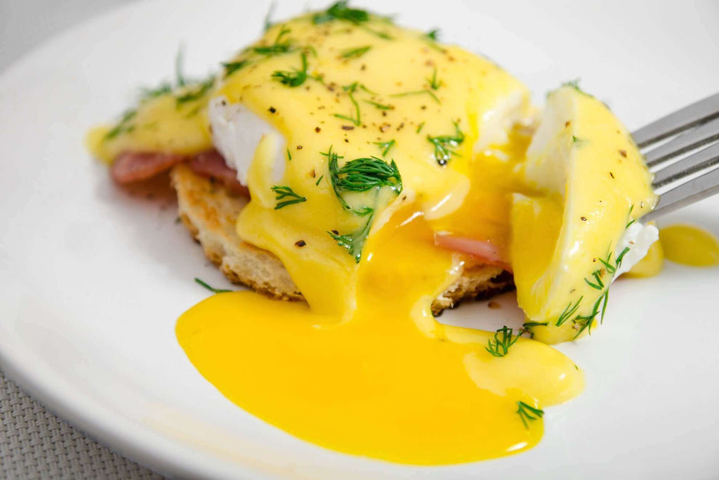 Delicious eggs Benedict topped with dill and hollandaise sauce, featuring a runny yolk on a toasted English muffin.