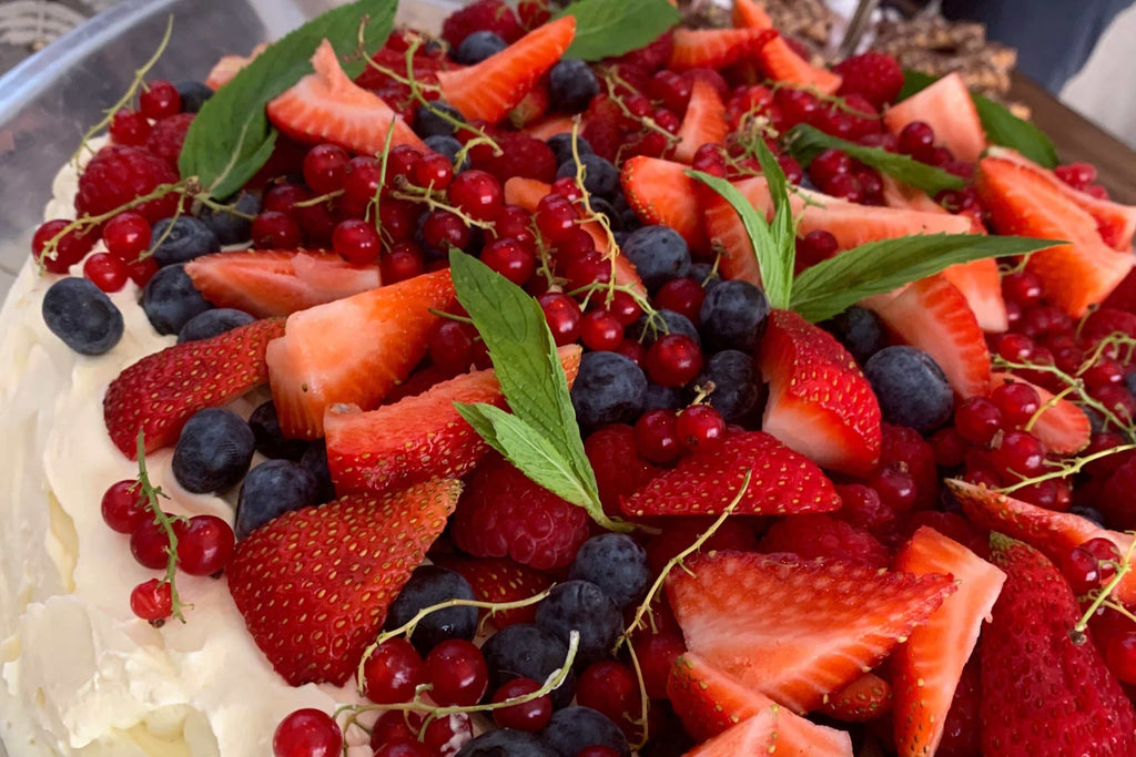 Delicious pavlova topped with fresh strawberries, blueberries, and red currants, garnished with mint leaves.