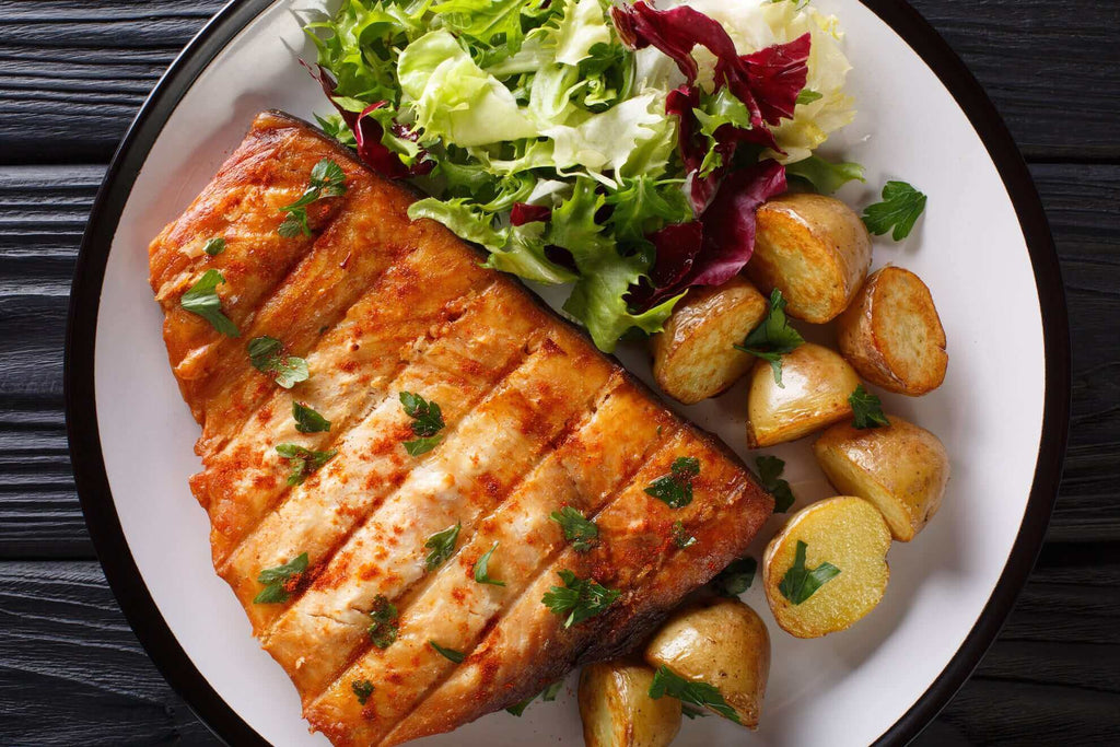 Grilled salmon served with fresh salad and roasted baby potatoes on a white plate.