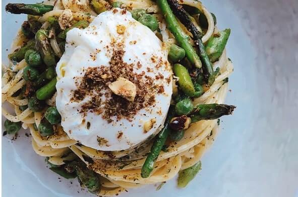 Plate of spaghetti topped with poached egg, green peas, asparagus, and Dukkah seasoning.