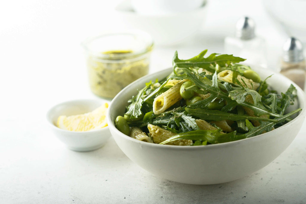 Bowl of penne pasta with arugula and preserved lemon paste on a light background.