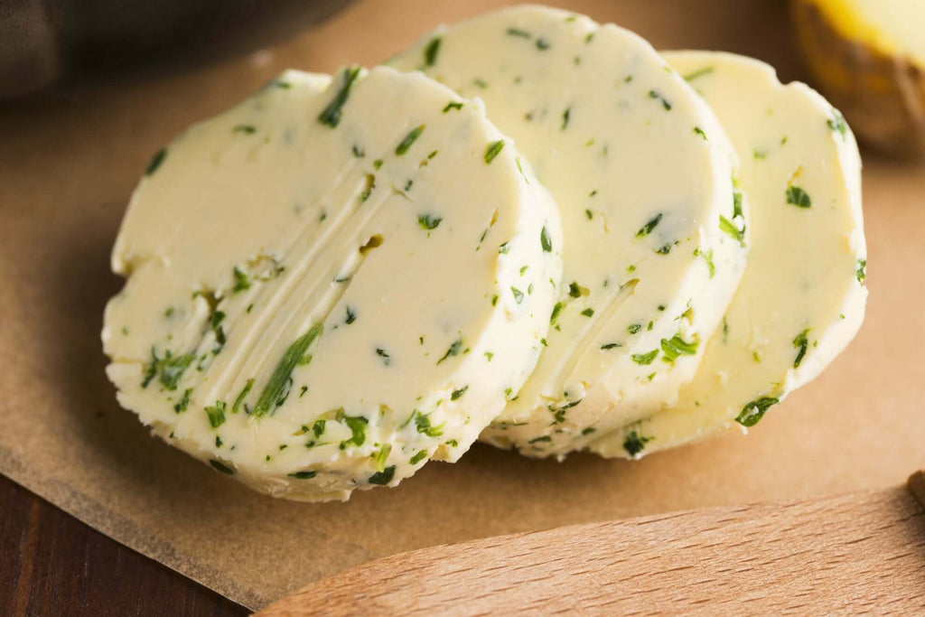 Slices of lemon herb butter with fresh herbs on a wooden surface, perfect for gourmet cooking and flavoring dishes.