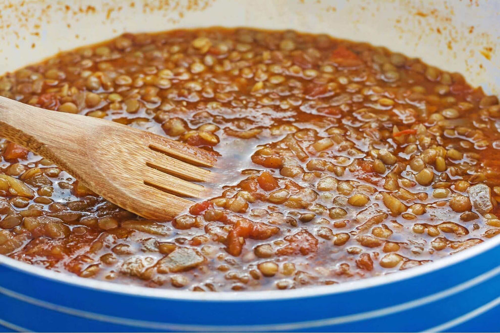 Close-up of hearty vegetable stew with lentils, featuring a wooden spoon, ideal for cozy meals.