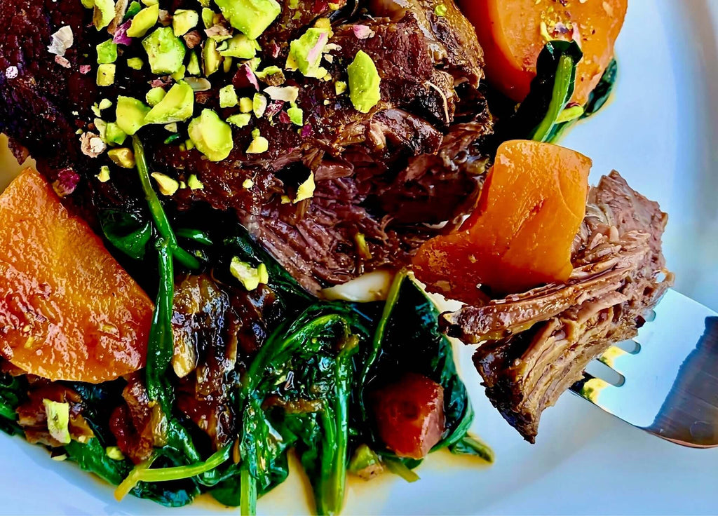 Delicious braised beef cheeks served with spinach, carrots, and topped with chopped pistachios.