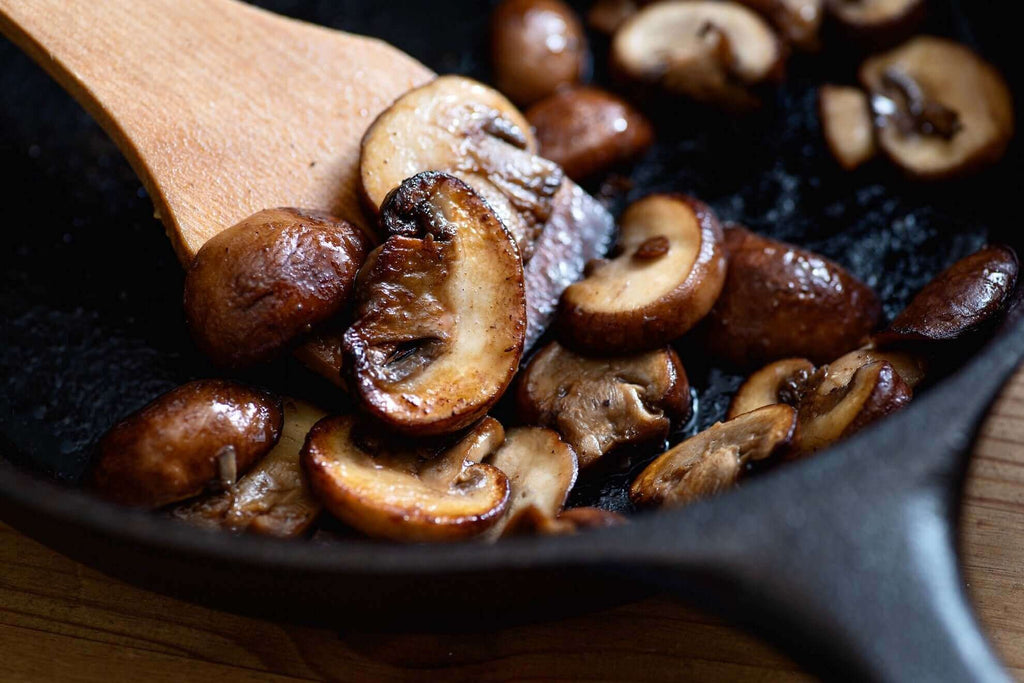 Sautéed mushrooms in a cast iron skillet with a wooden spatula, showcasing a delicious skillet recipe.