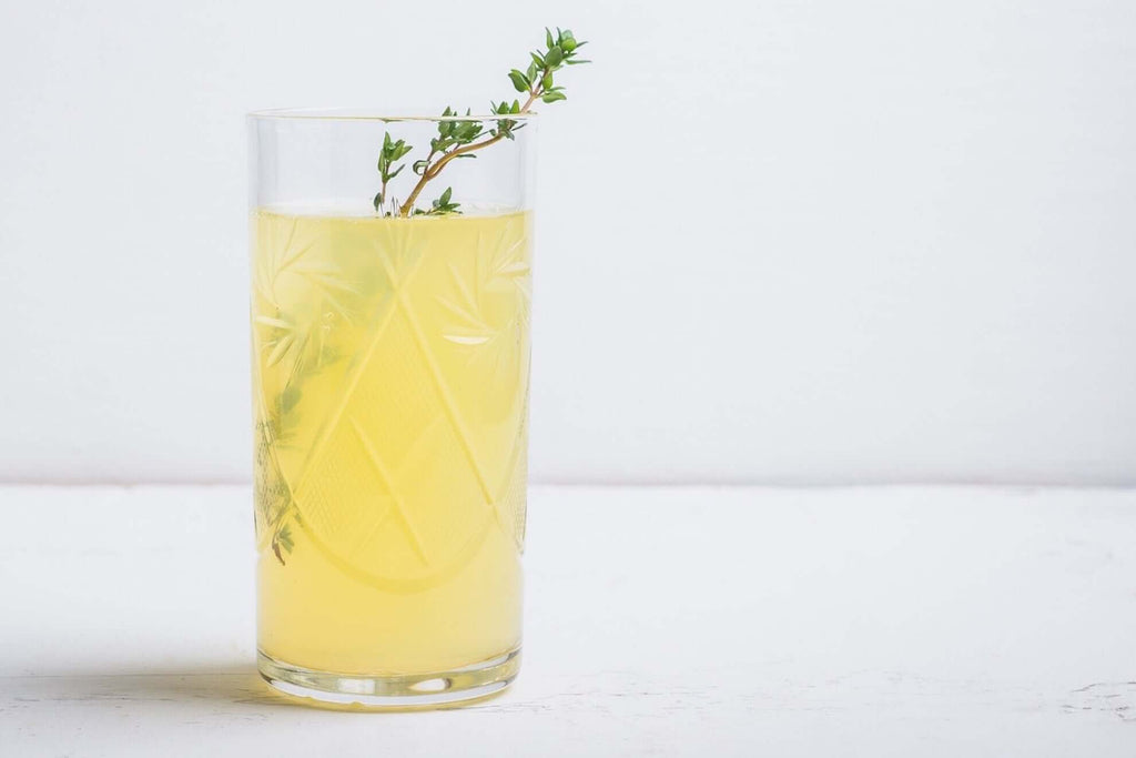 Glass of refreshing Meyer lemon cocktail garnished with thyme against a light background.