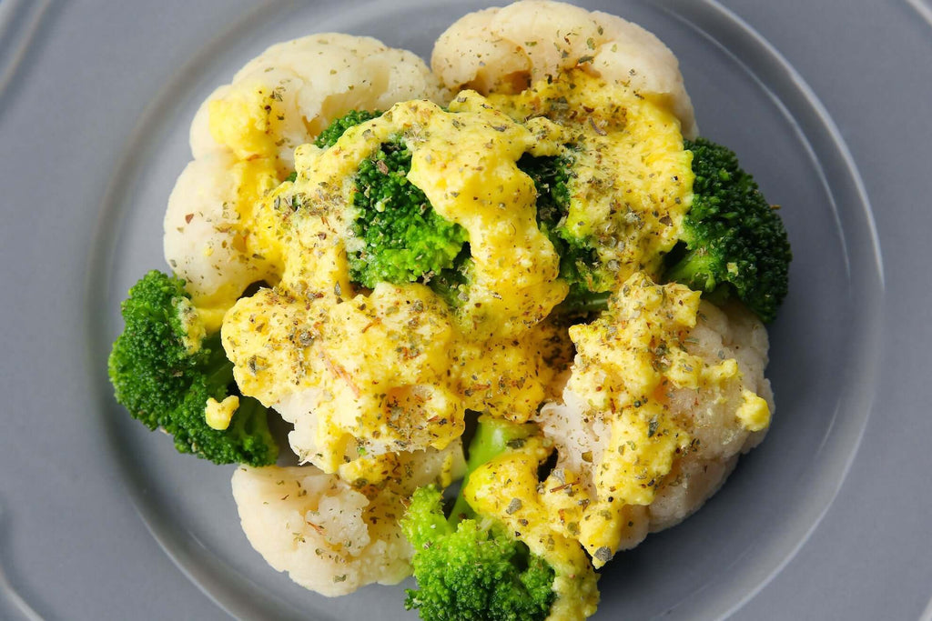 Steamed broccoli and cauliflower topped with creamy cheese sauce on a gray plate.