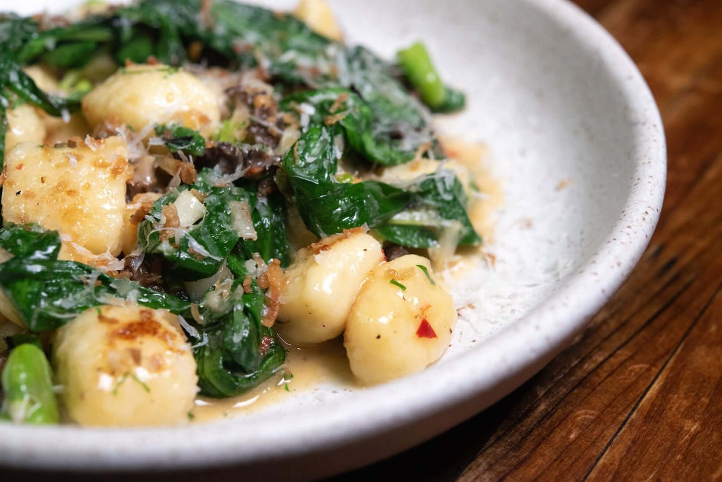 Vegetable gnocchi with fresh spinach in a creamy sauce, garnished with cheese and herbs in a rustic serving bowl.