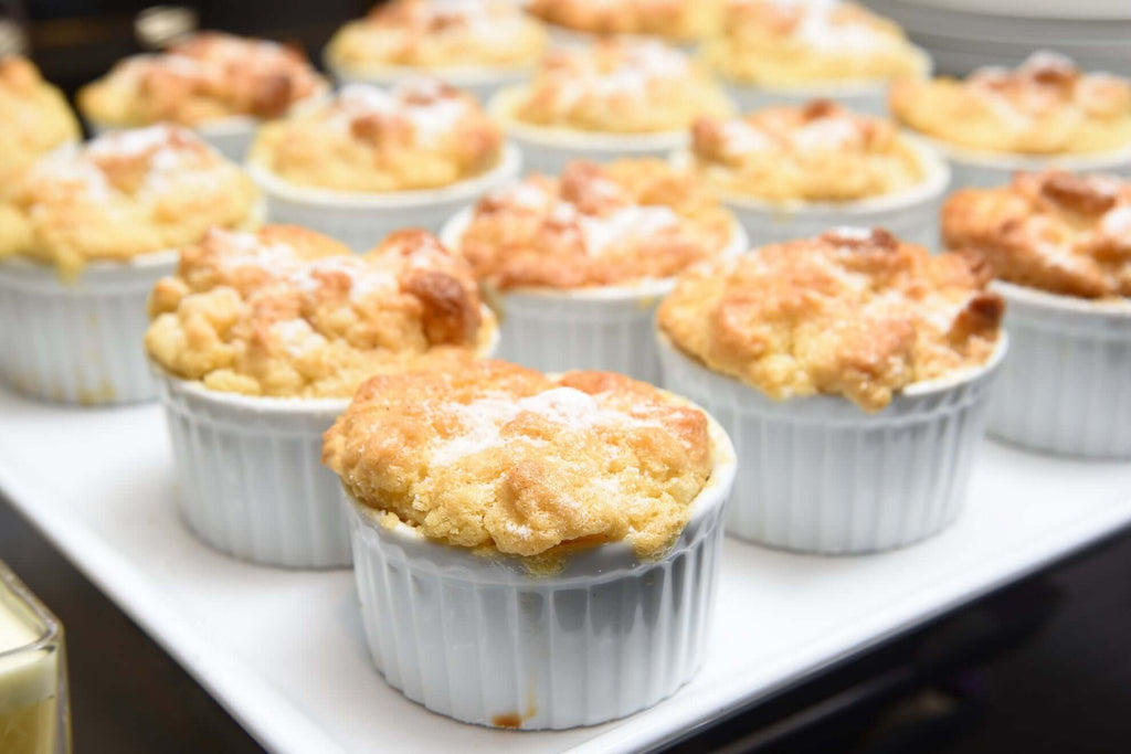 Freshly baked Meyer lemon bread pudding soufflés in white ramekins, topped with a dusting of powdered sugar.