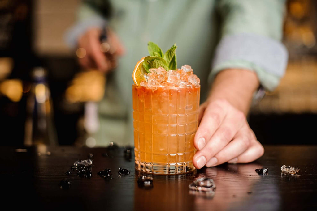 Refreshing bourbon cocktail garnished with mint and ice, served in a stylish glass on a wooden bar.