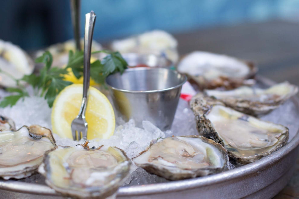 Freshly shucked oysters on ice served with lemon and dipping sauce for gourmet seafood enjoyment.