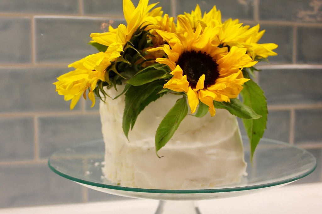 Berry layer cake topped with vibrant sunflowers, beautifully displayed on a glass cake stand.