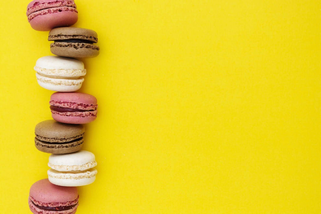 Colorful California macarons in various flavors arranged on a vibrant yellow background.