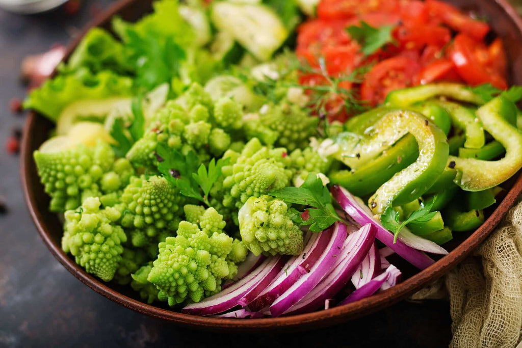 A colorful bowl of fresh, vibrant vegetables including romanesco, bell peppers, lettuce, and tomatoes.