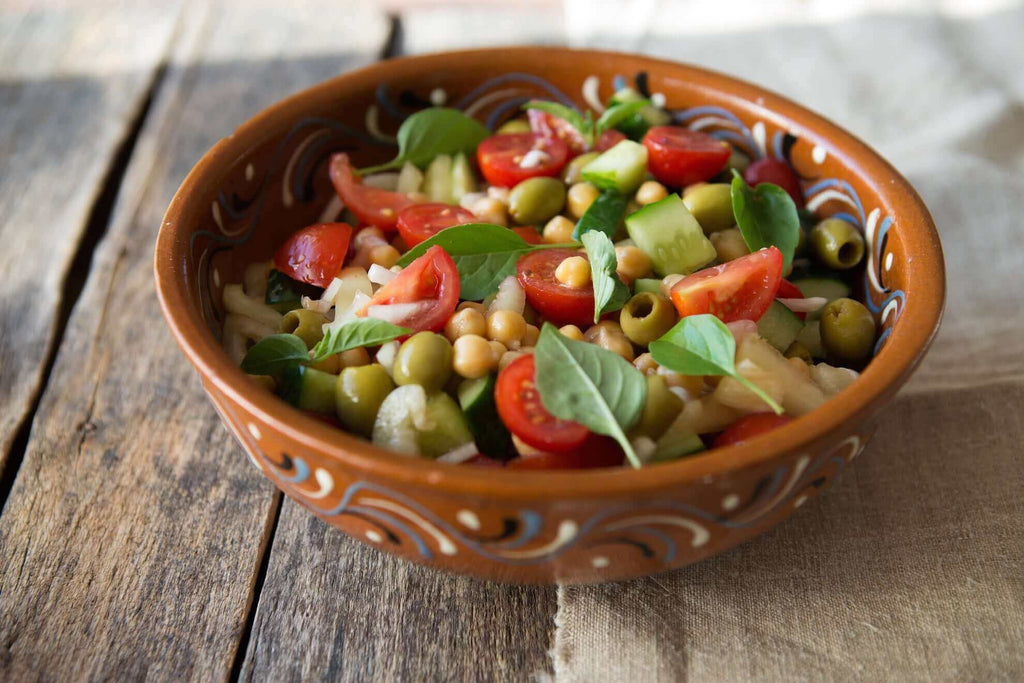 Colorful chickpea salad with cherry tomatoes, cucumbers, olives, and fresh basil in a decorative bowl.