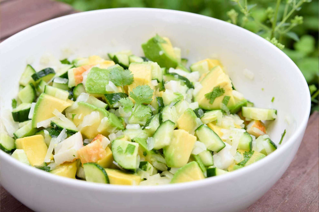 Fresh salad with cucumbers, avocado, and herbs garnished with cilantro in a white bowl.