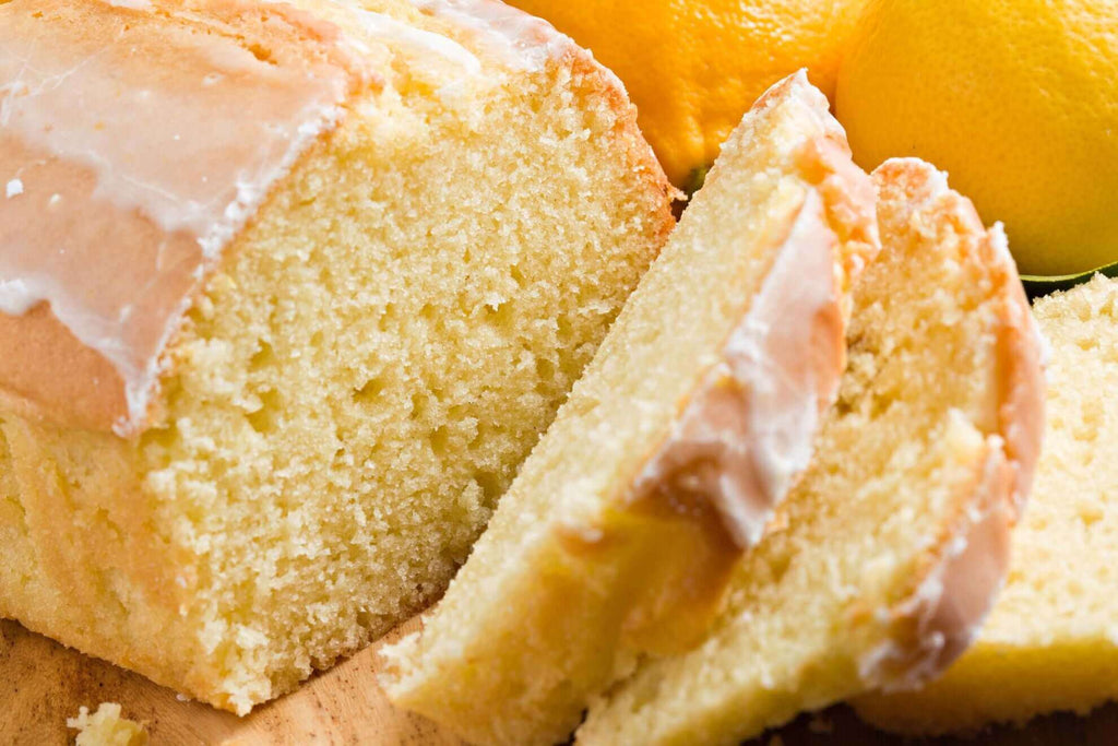 Sliced lemon pound cake with a glossy glaze, surrounded by fresh lemons on a wooden surface.