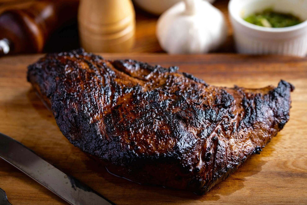 Juicy, grilled tri-tip steak on a wooden cutting board with seasoning and garlic in the background.