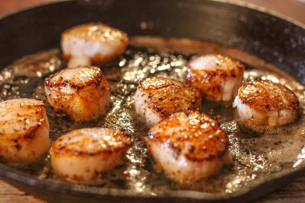 Grilled scallops sizzling in a hot cast iron skillet with butter and spices.