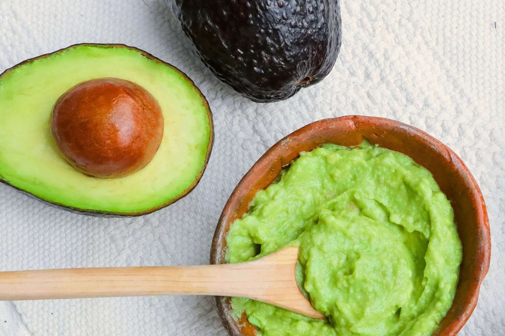 Bowl of creamy guacamole with ripe avocado halves and a wooden spoon, showcasing a simple one-ingredient recipe.