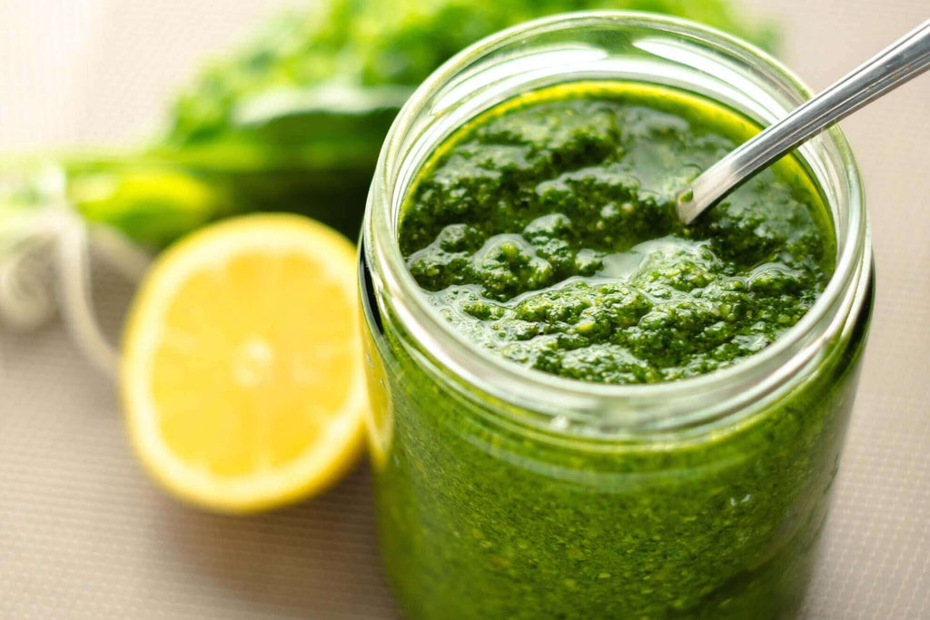 Jar of vibrant green pesto next to a slice of lemon, showcasing fresh ingredients for a flavorful dish.