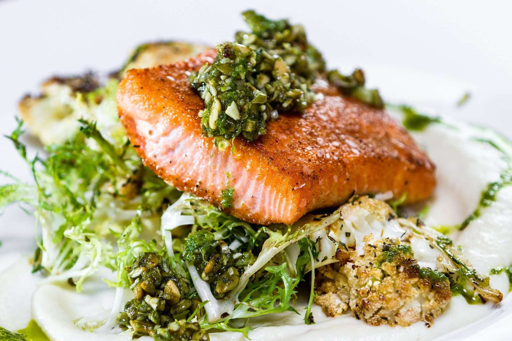 Crispy salmon fillet topped with herb salsa on a bed of greens and roasted cauliflower.