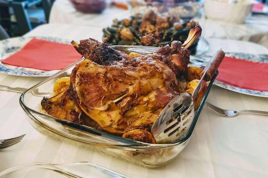 Roasted lamb shoulder served with golden potatoes in a glass dish on a dining table.