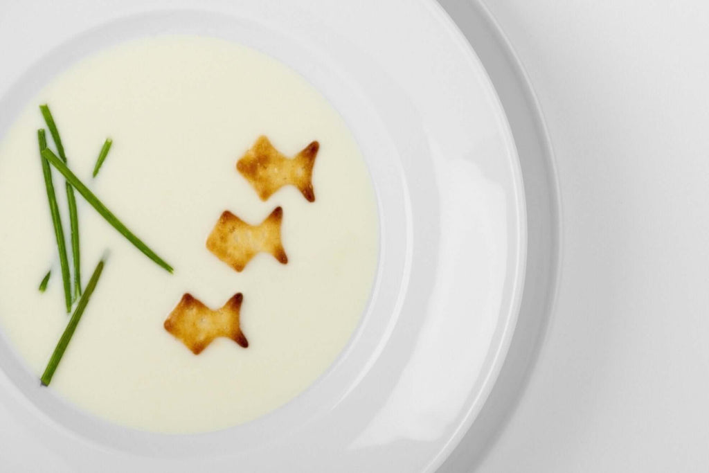 Creamy Vichyssoise soup with fish-shaped crackers and chives on a white plate.